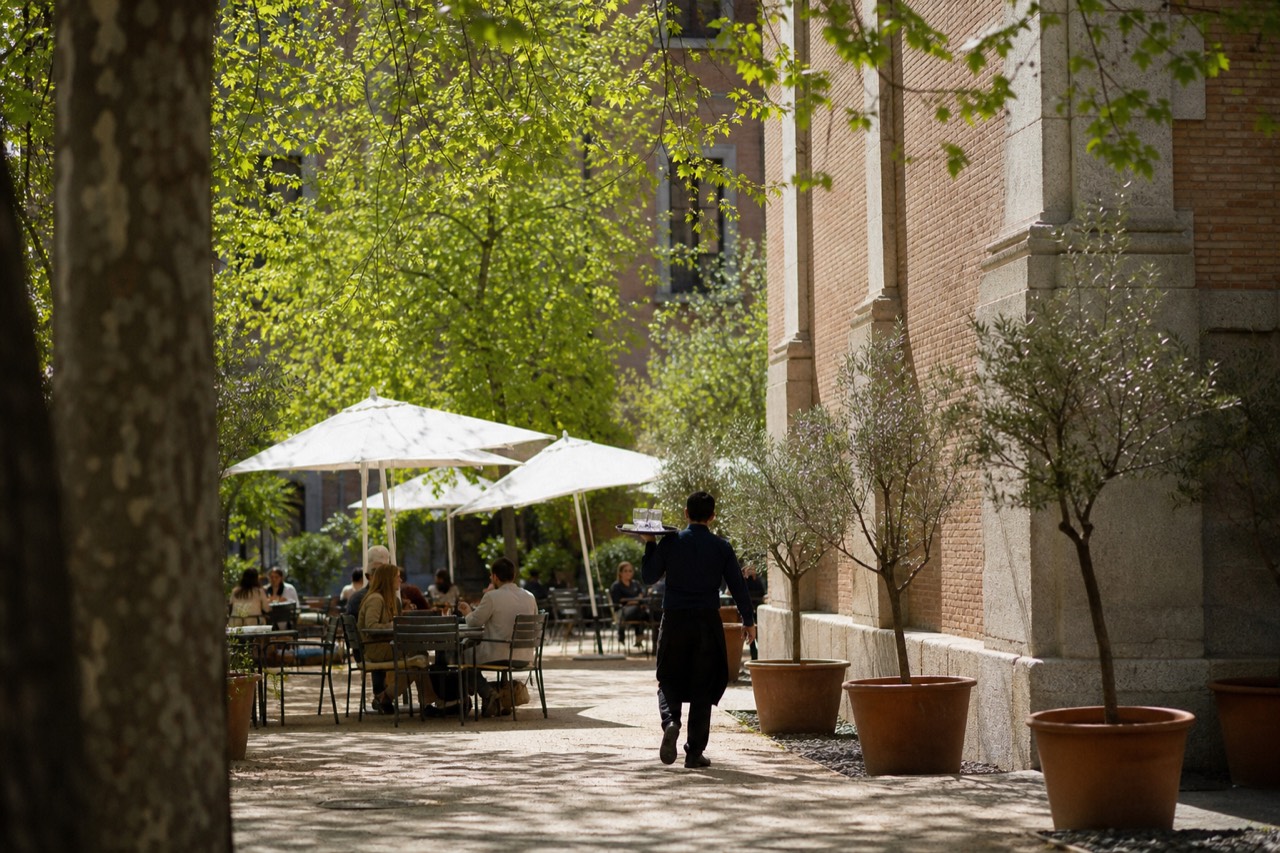 Pedestrians resting on a shaded plaza in front of a contemporary arts centre