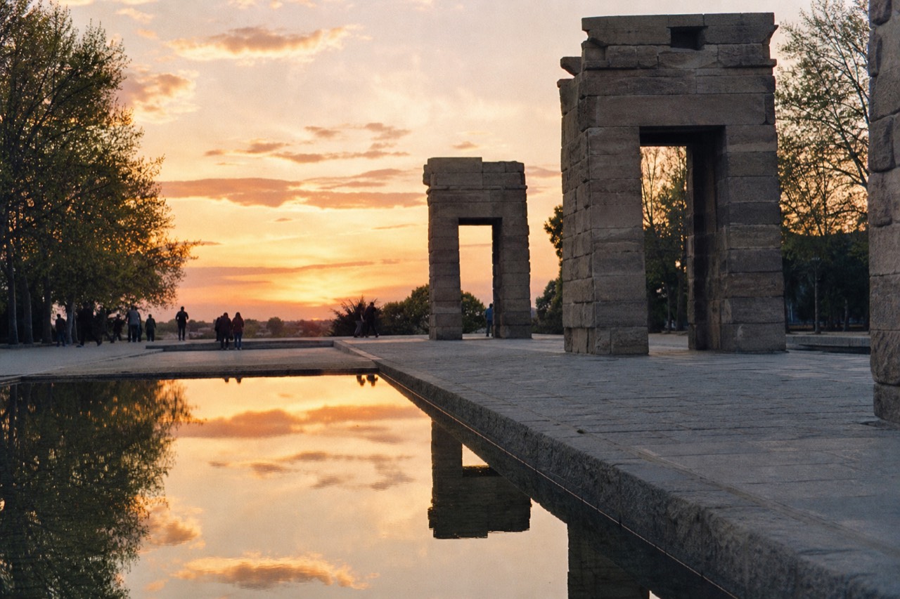An ancient stone gateway reflected in a still rectangular pool at sunset