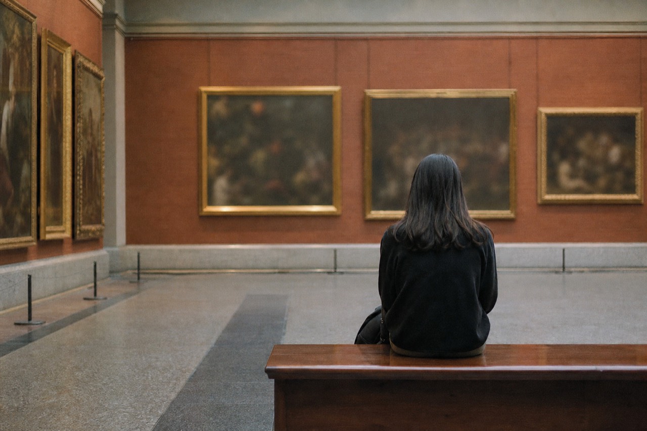 A tall museum gallery with stone carvings on plinths and visitors reading labels