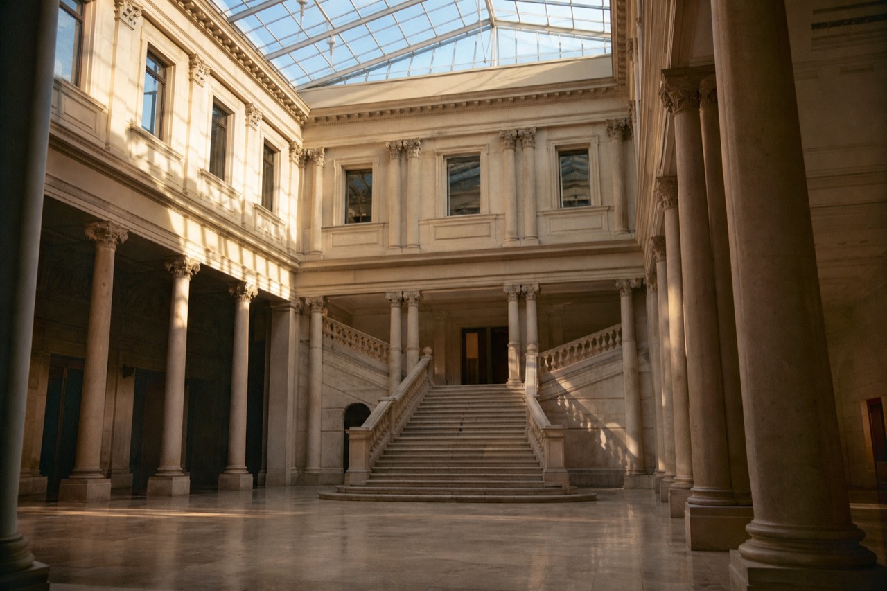 Wide gravel courtyard in front of a long pale stone palace facade in low afternoon light