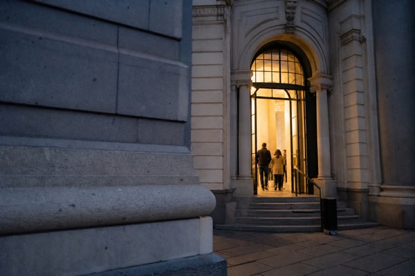 Modern stone museum gallery with tapestries and display cases lit from a tall glazed wall